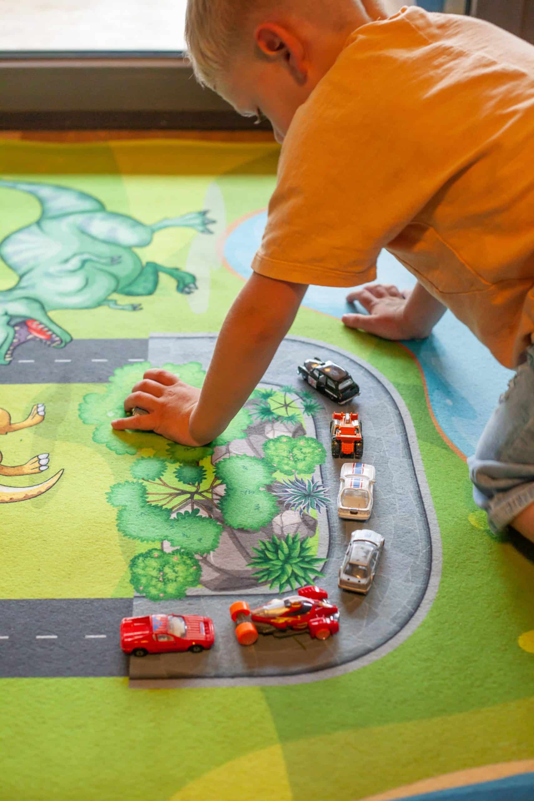 Kind spielt mit Spielzeug-Autos auf Spielteppich Straße